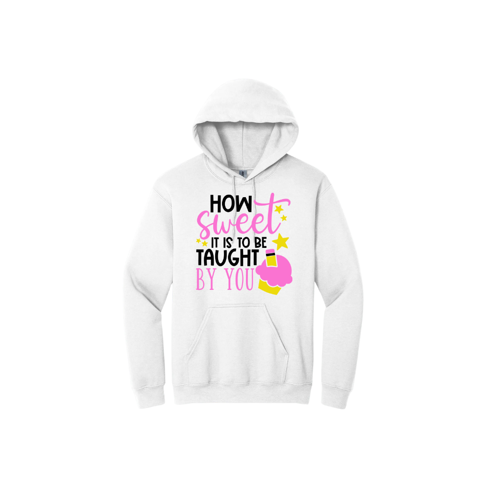 White unisex hoodie featuring black and pink text that reads 'How sweet it is to be taught by you' alongside graphics of starts and a cupcake with a pencil stuck in it.